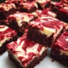 Red velvet brownies with cream cheese swirl cut into squares, showing fudgy texture and marbled cream cheese throughout, displayed on white parchment paper