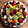 Easter Egg Fruit Pizza on a white platter with colorful fresh fruit including strawberries, blueberries, kiwi, and mandarin oranges arranged on cream cheese frosting over a sugar cookie crust