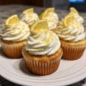 lemon limoncello cupcakes topped with swirled lemon buttercream frosting and garnished with fresh lemon zest on a white cake stand