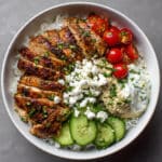 chicken shawarma bowl with sliced marinated chicken, jasmine rice, cherry tomatoes, cucumber, hummus, tzatziki sauce, and fresh parsley garnish