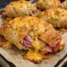 brown baked ham and cheese croissants on a white plate, with melted cheese visible and sesame seeds sprinkled on top
