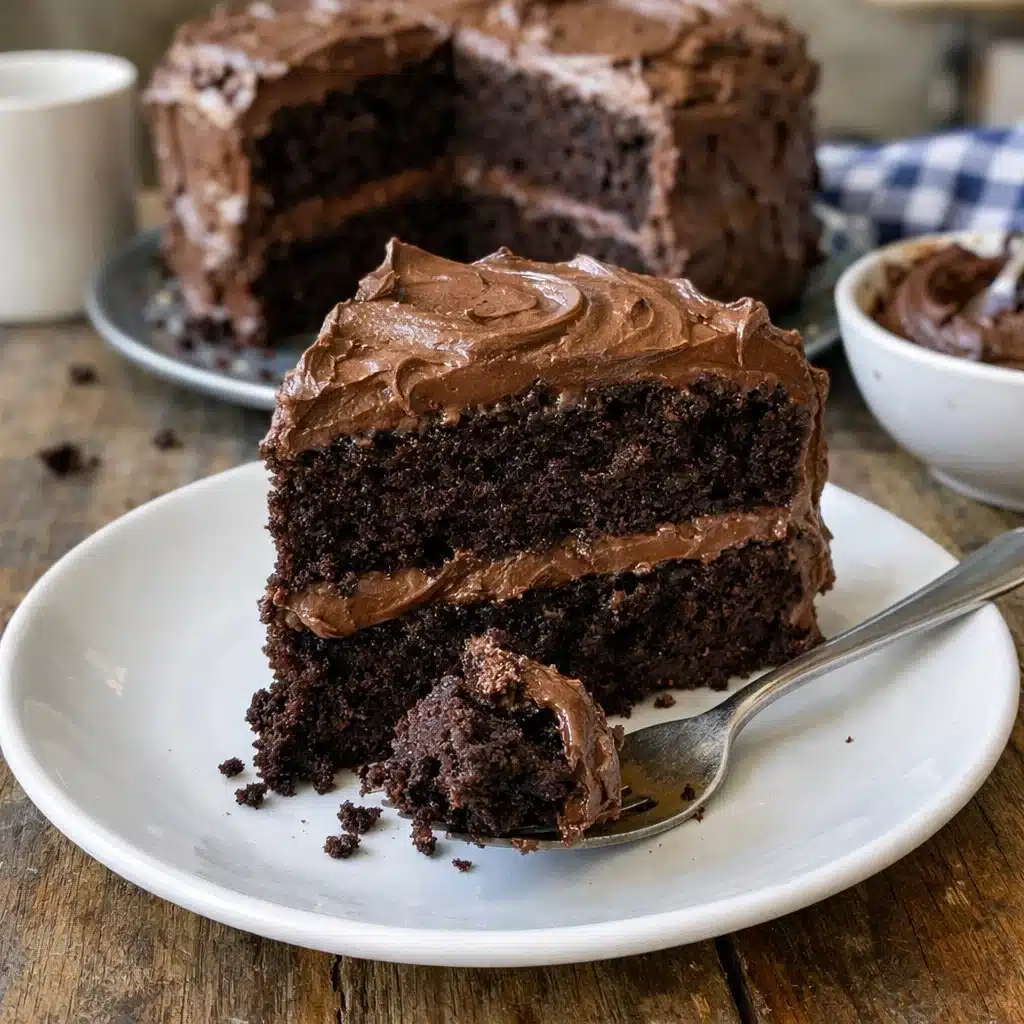 A slice of moist chocolate sour cream cake on a white plate with a fork, showing the tender crumb and rich dark color