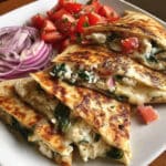 Golden crispy quesadilla cut into wedges showing melted cheese and colorful vegetable filling with spinach, tomatoes, and red onions on a white plate