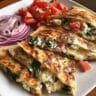 Golden crispy quesadilla cut into wedges showing melted cheese and colorful vegetable filling with spinach, tomatoes, and red onions on a white plate
