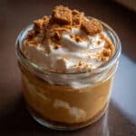 Creamy Biscoff pudding served in clear glasses with smooth swirl top and spoon lifting thick caramel-colored pudding
