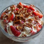 Bowl of strawberry crackle salad with creamy white filling, fresh red strawberries, and golden caramelized pretzel pecan crunch on top