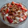 Bowl of strawberry crackle salad with creamy white filling, fresh red strawberries, and golden caramelized pretzel pecan crunch on top